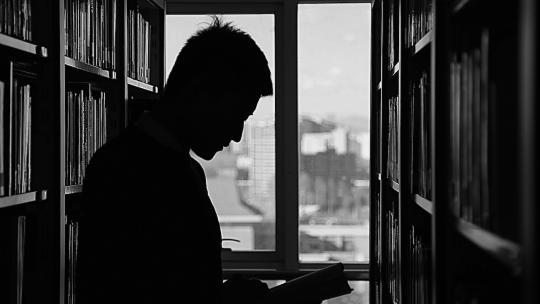 Persona a contraluz leyendo un libro en la biblioteca.