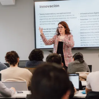 En una clase de la UNIE, la docente imparte clase del área de matemáticas con la ayuda de una pizarra digital. Los estudiantes sentados y atentos siguen la clase con sus portátiles y se preparan para la profesión y la vida.