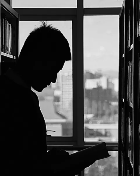 Persona a contraluz leyendo un libro en la biblioteca.