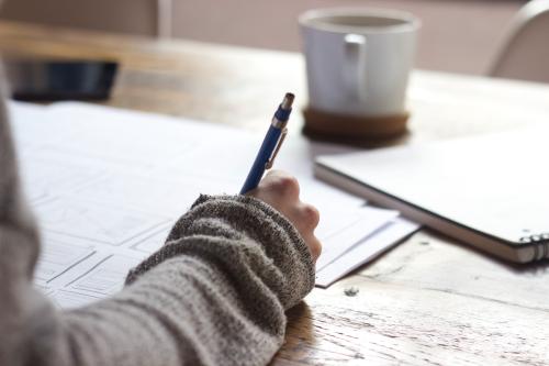 Persona escribiendo con un café en la mesa.