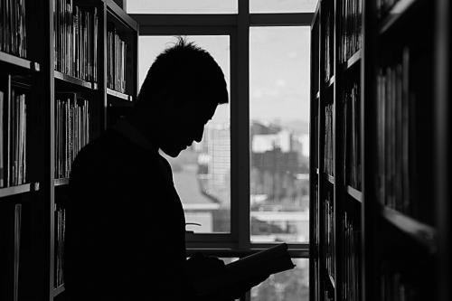 Persona a contraluz leyendo un libro en la biblioteca.